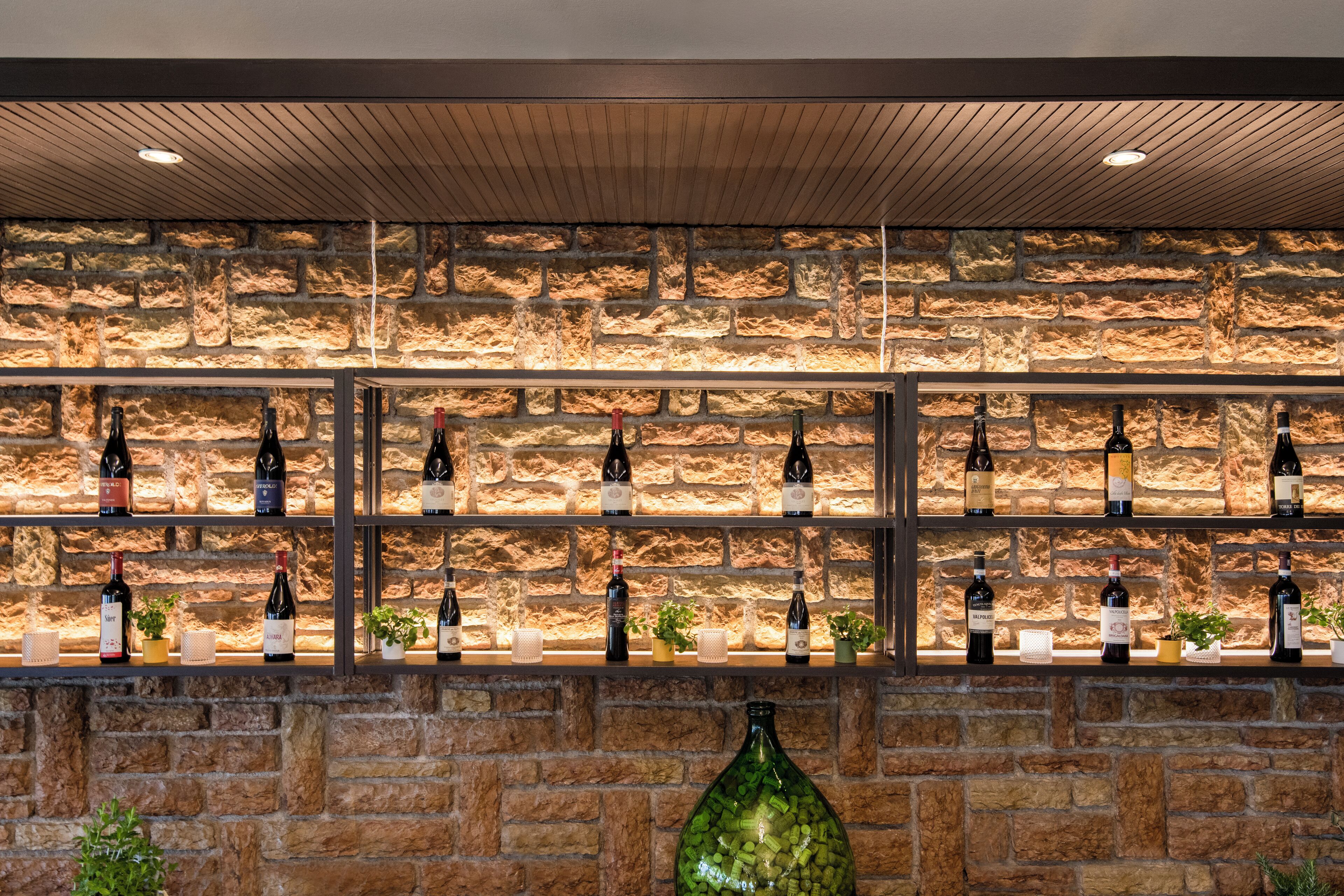 A bar area with shelves of wine bottles against a stone wall backdrop.