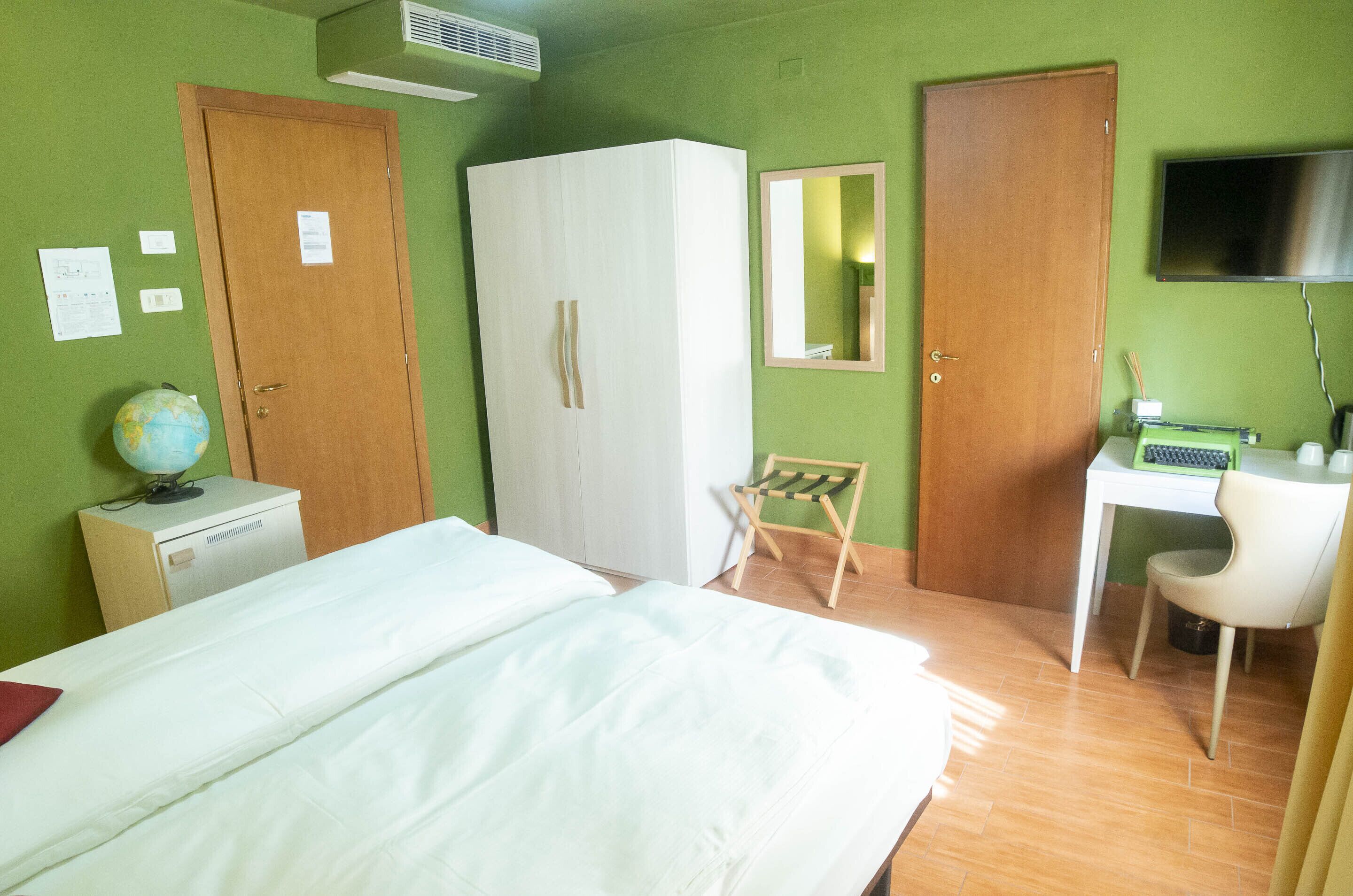 A hotel room with a bed, wardrobe, desk, chair, and a television on the wall.