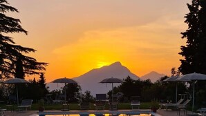 Una piscina con sillas de descanso y sombrillas, rodeada de árboles y una montaña al fondo.