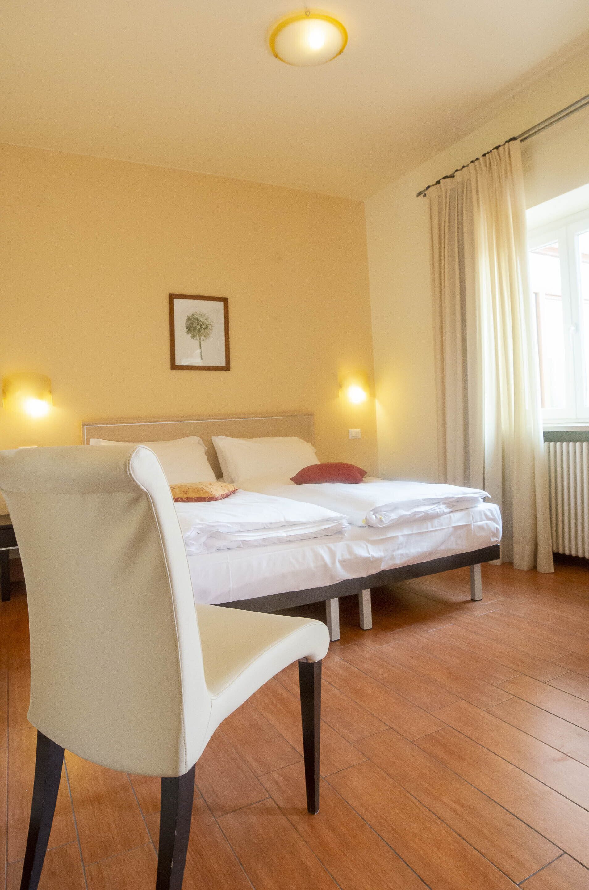 A hotel room with a bed, a chair, a picture on the wall, and two wall-mounted lamps.