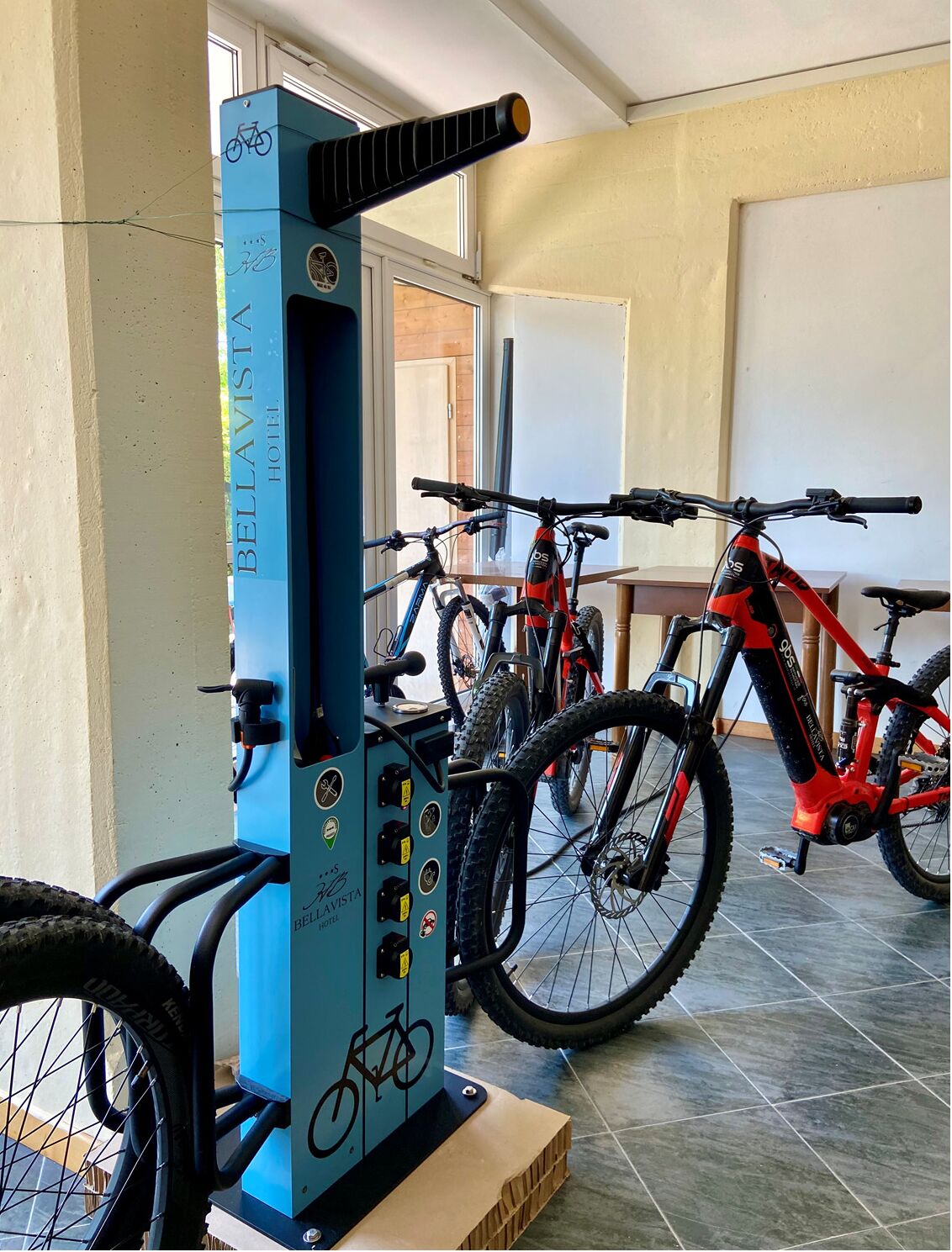 A bike rental station with a blue machine, two bicycles, and a wooden table in a hotel lobby.