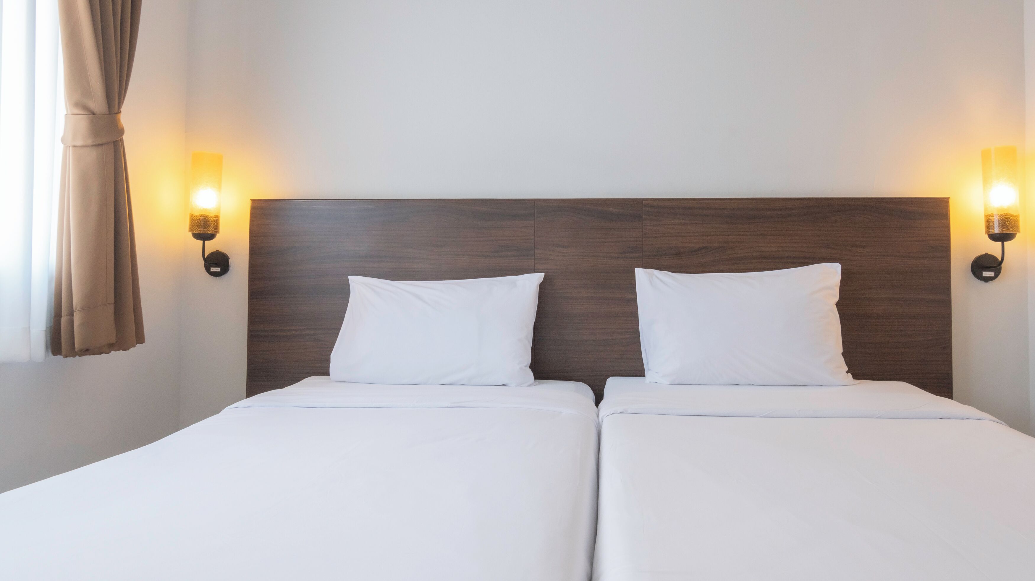 Una cama doble con sábanas blancas, dos almohadas y un cabecero de madera. Hay dos lámparas de pared a cada lado de la cama.