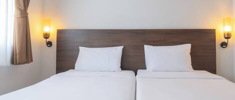 Una cama doble con sábanas blancas, dos almohadas y un cabecero de madera. Hay dos lámparas de pared a cada lado de la cama.