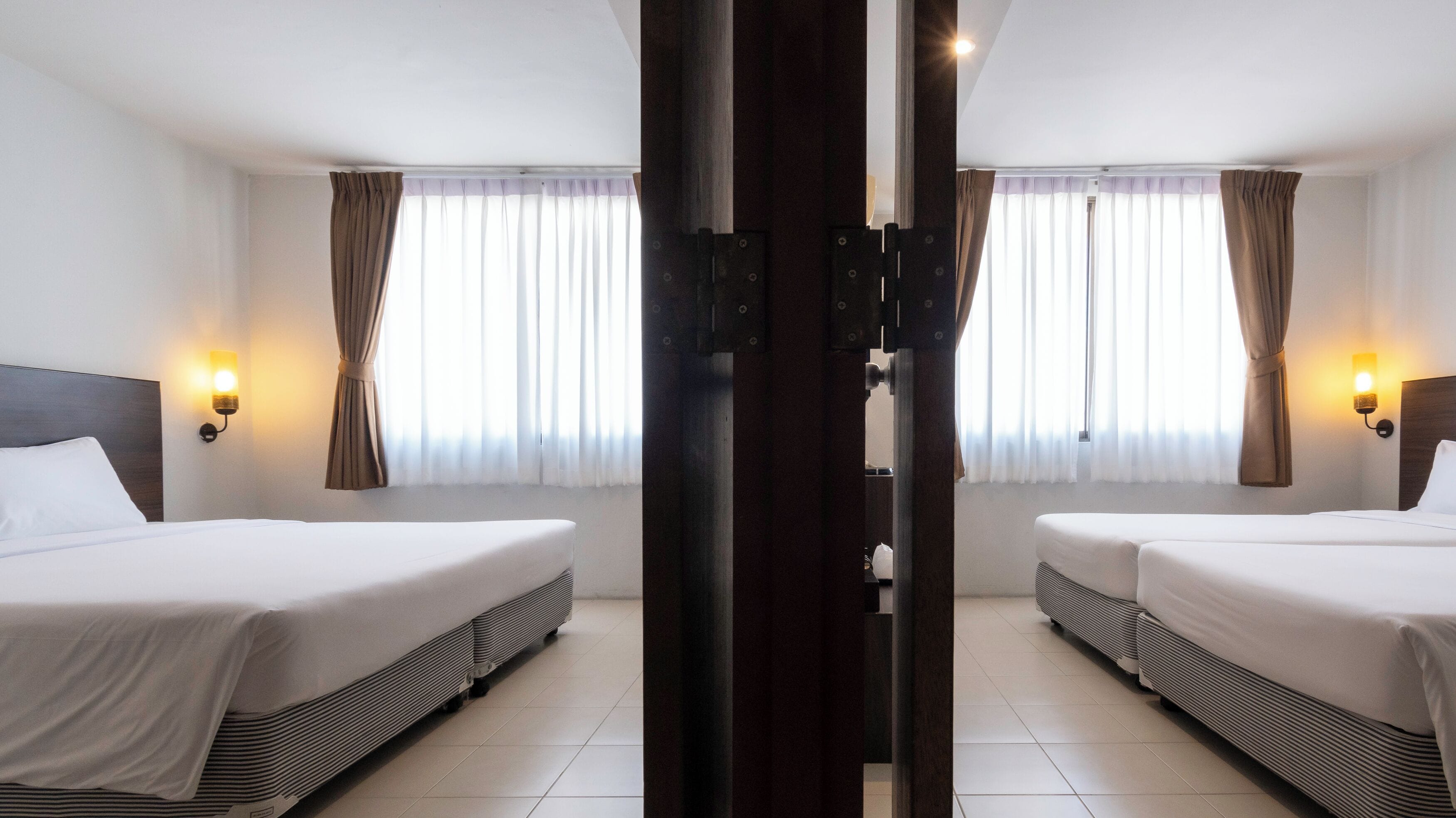 A hotel room with two beds, a wooden pillar, and curtains.