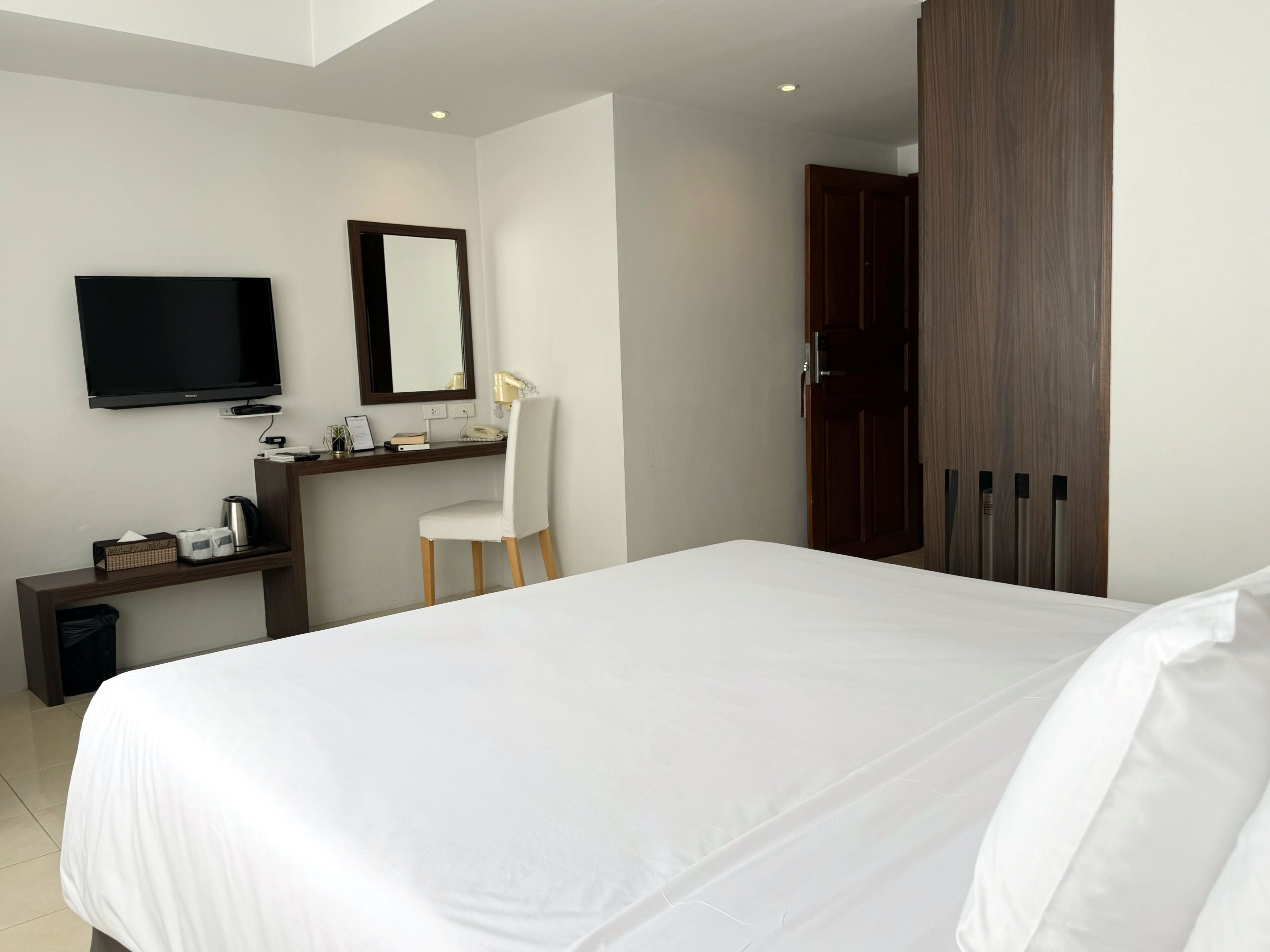 Una habitación de hotel con una cama grande, un escritorio con silla, televisión y armario.