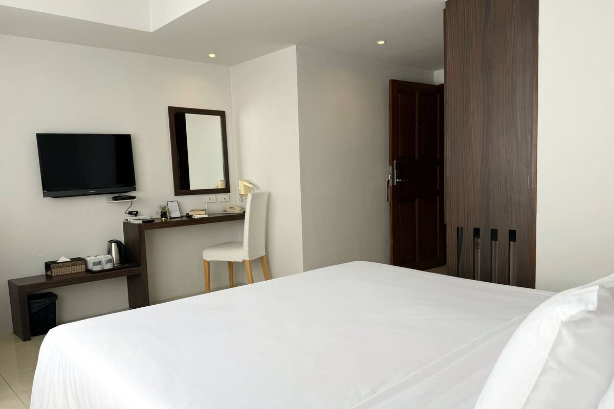 A hotel room with a large bed, a desk with a chair, a television, and a wardrobe.