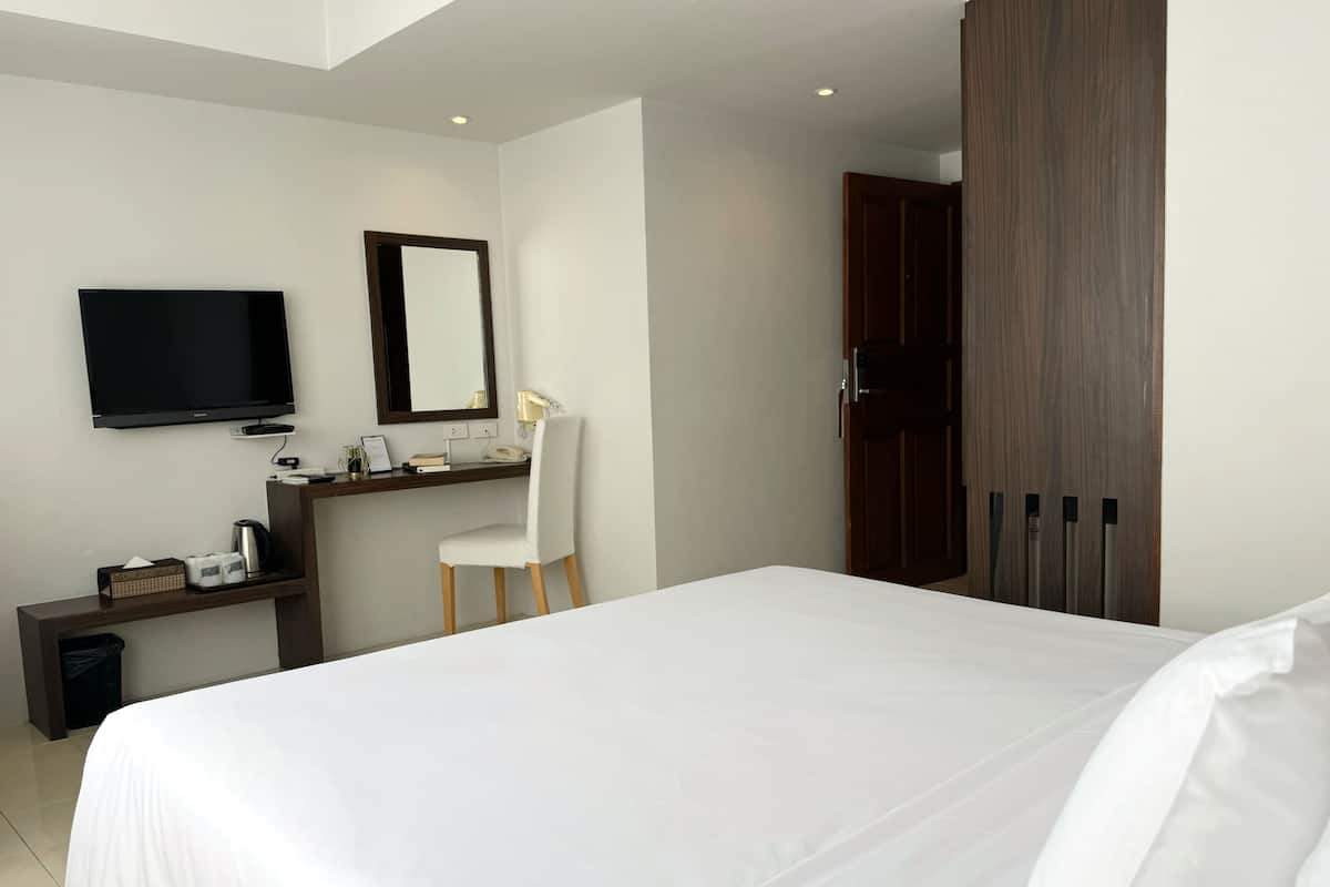 A hotel room with a large bed, a desk with a chair, a television, and a wardrobe.
