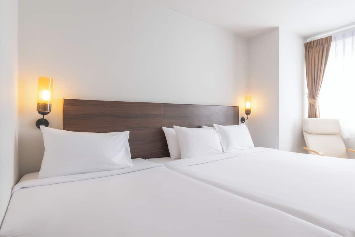 A hotel room with a double bed, two bedside tables, a chair, and a window with curtains.