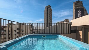 Una piscina en la azotea con vistas a edificios altos al fondo.