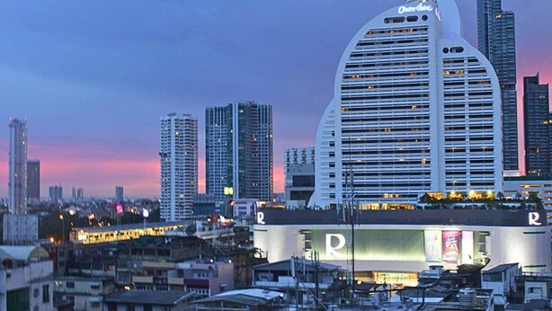 Un hotel con un techo curvo distintivo y una gran 'R' en la fachada, rodeado de edificios altos y un paisaje urbano al atardecer.