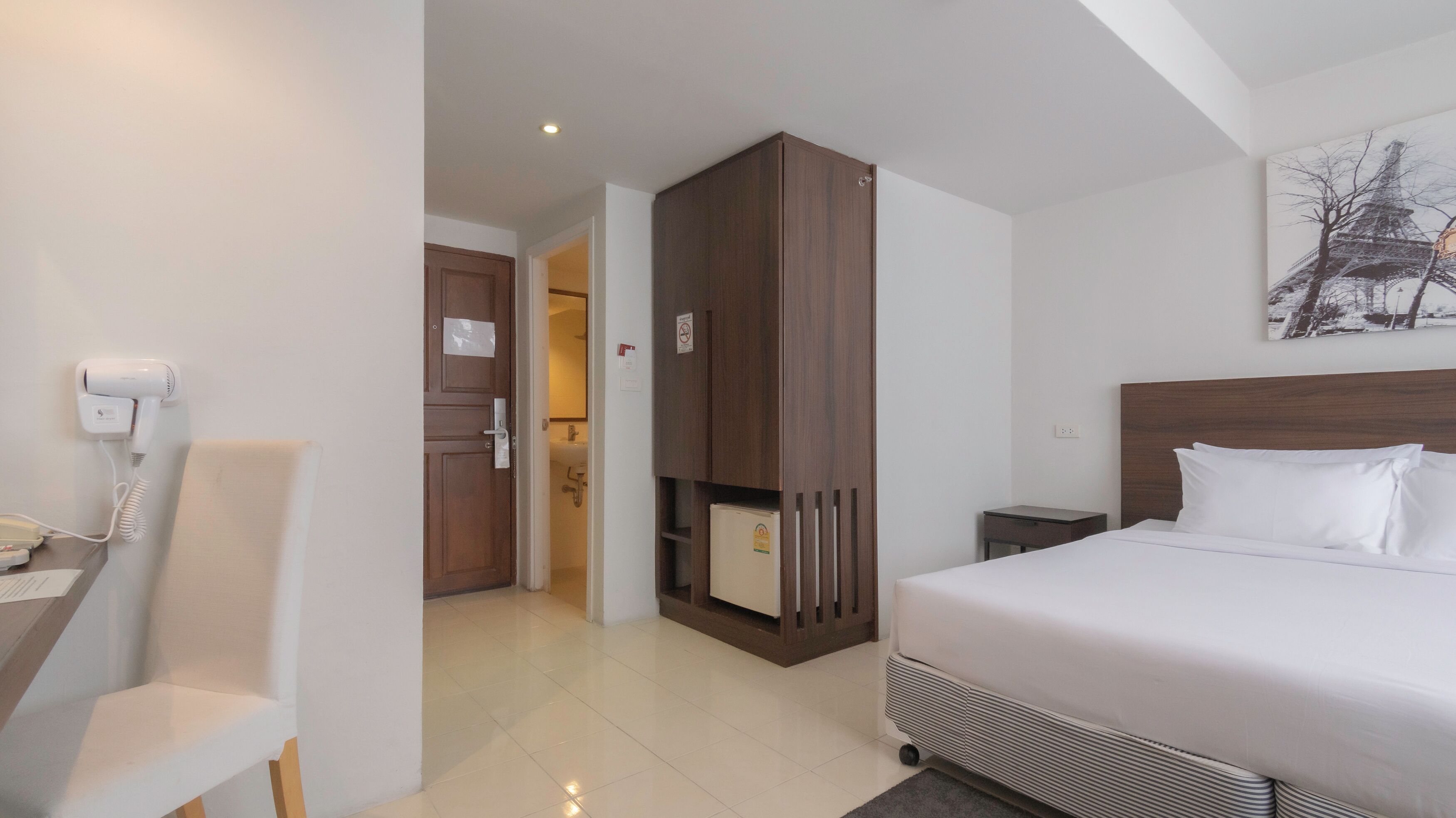 Habitación de hotel con cama, escritorio con teléfono, armario y un cuadro de la Torre Eiffel.
