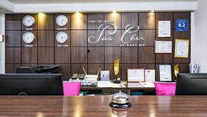 Una mesa de recepción con relojes que muestran la hora de Tokio, Bangkok, Londres y Nueva York, un certificado enmarcado y un panel de información digital.