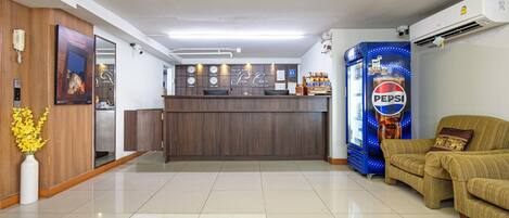 A hotel lobby with a reception desk, a Pepsi refrigerator, a sofa, and a vase with yellow flowers.