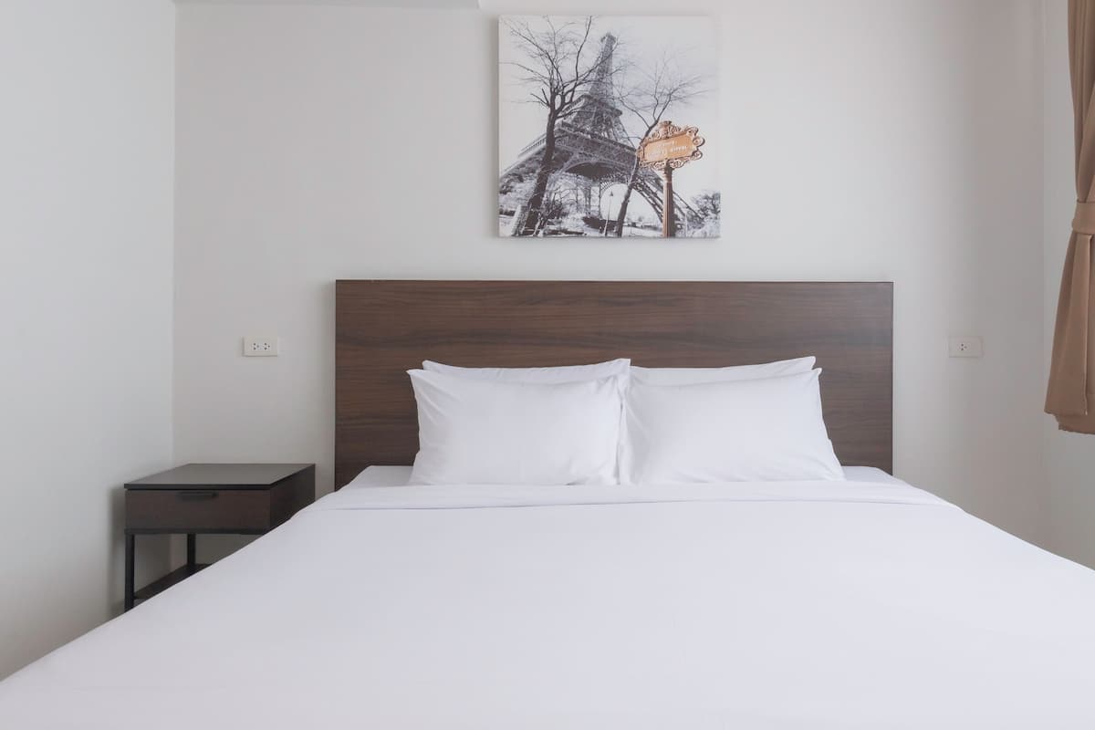 A hotel room with a large bed, a wooden headboard, a nightstand, and a wall-mounted picture of the Eiffel Tower.