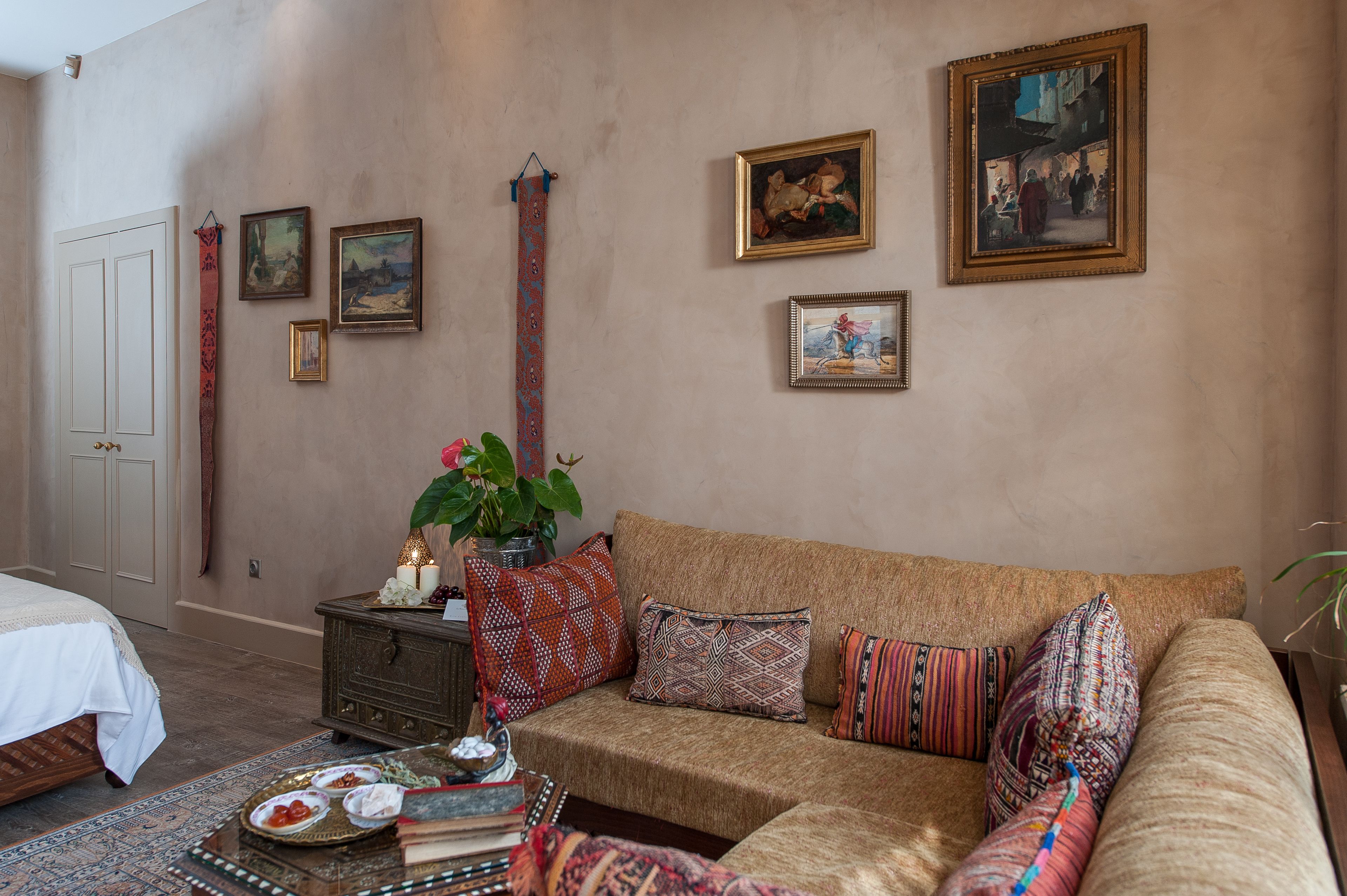 A cozy room with a sofa, a small table with decorative items, a bed, and a wall adorned with framed artwork.