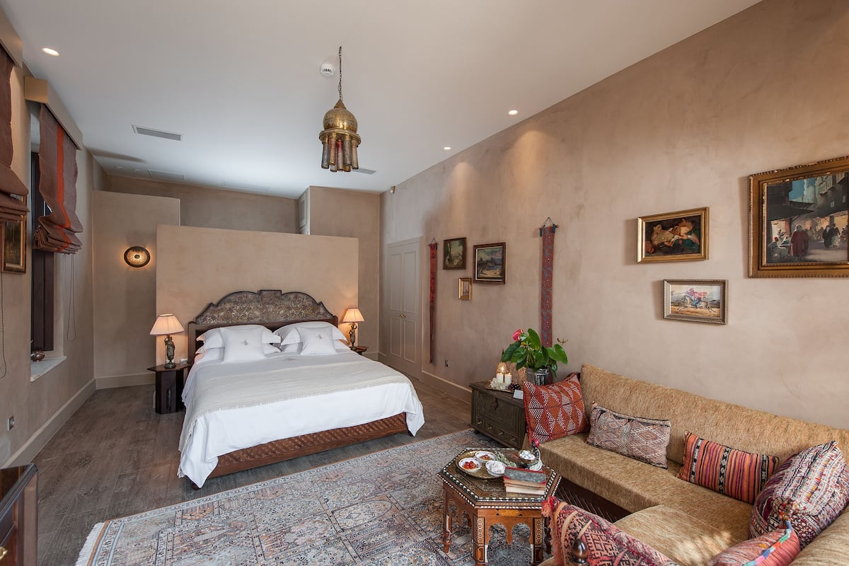 A bedroom with a large bed, a sofa, a small table with decorative items, and a hanging lamp.