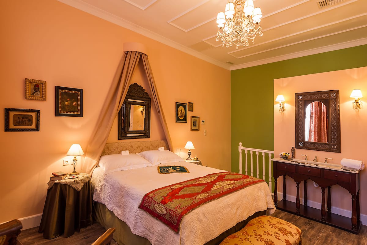 A hotel room with a bed, bedside lamps, a mirror, and a vanity with a sink.