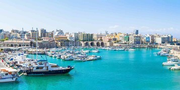 Una marina con numerose imbarcazioni ormeggiate, circondata da un panorama urbano con diversi edifici.