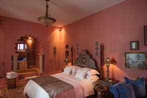 A bedroom with a bed, a nightstand, a lamp, a mirror, and a wall with decorative items. - La Maison Ottomane (Chania)