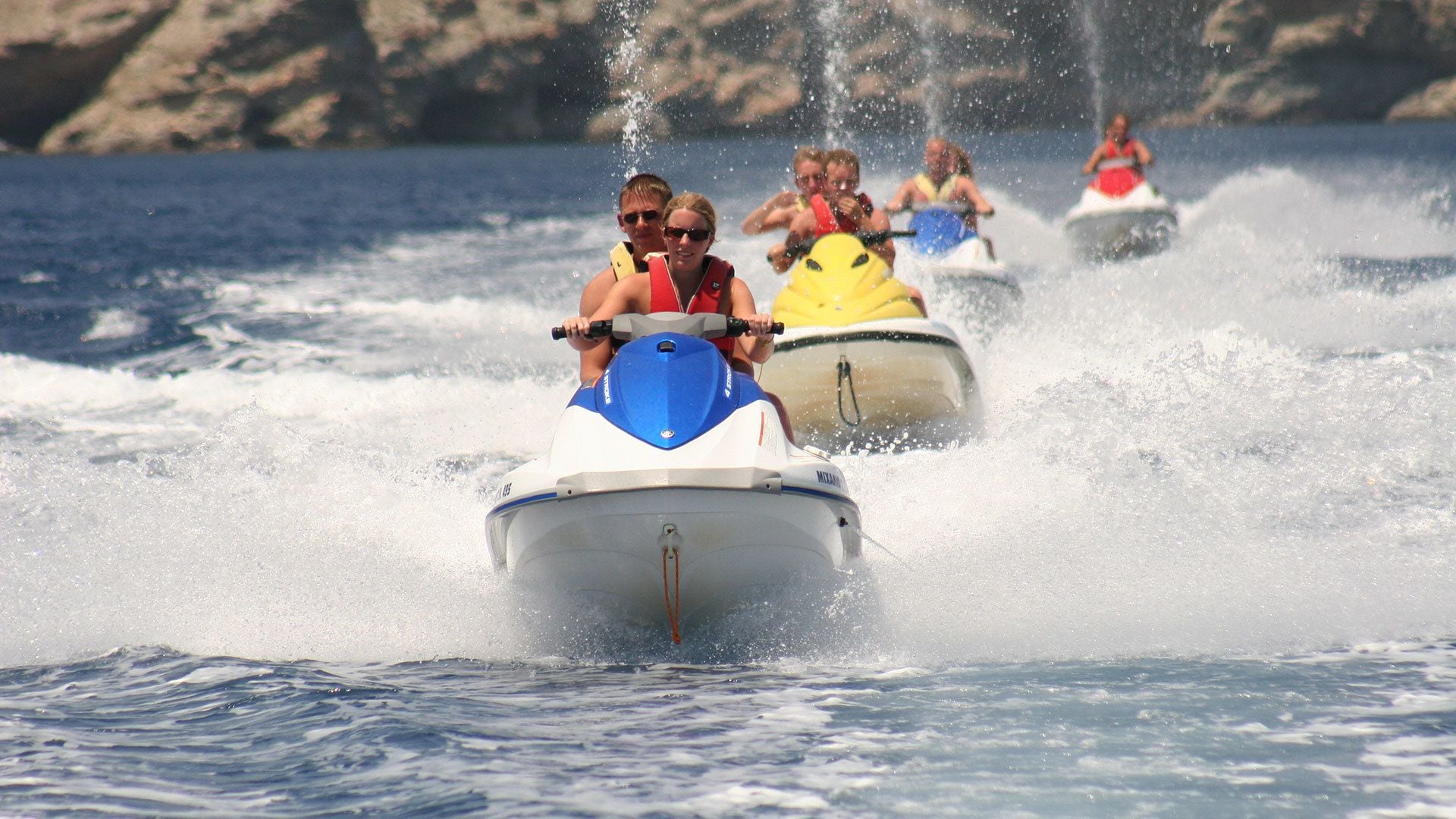 People jet-skiing on a body of water with waves created by the boats.