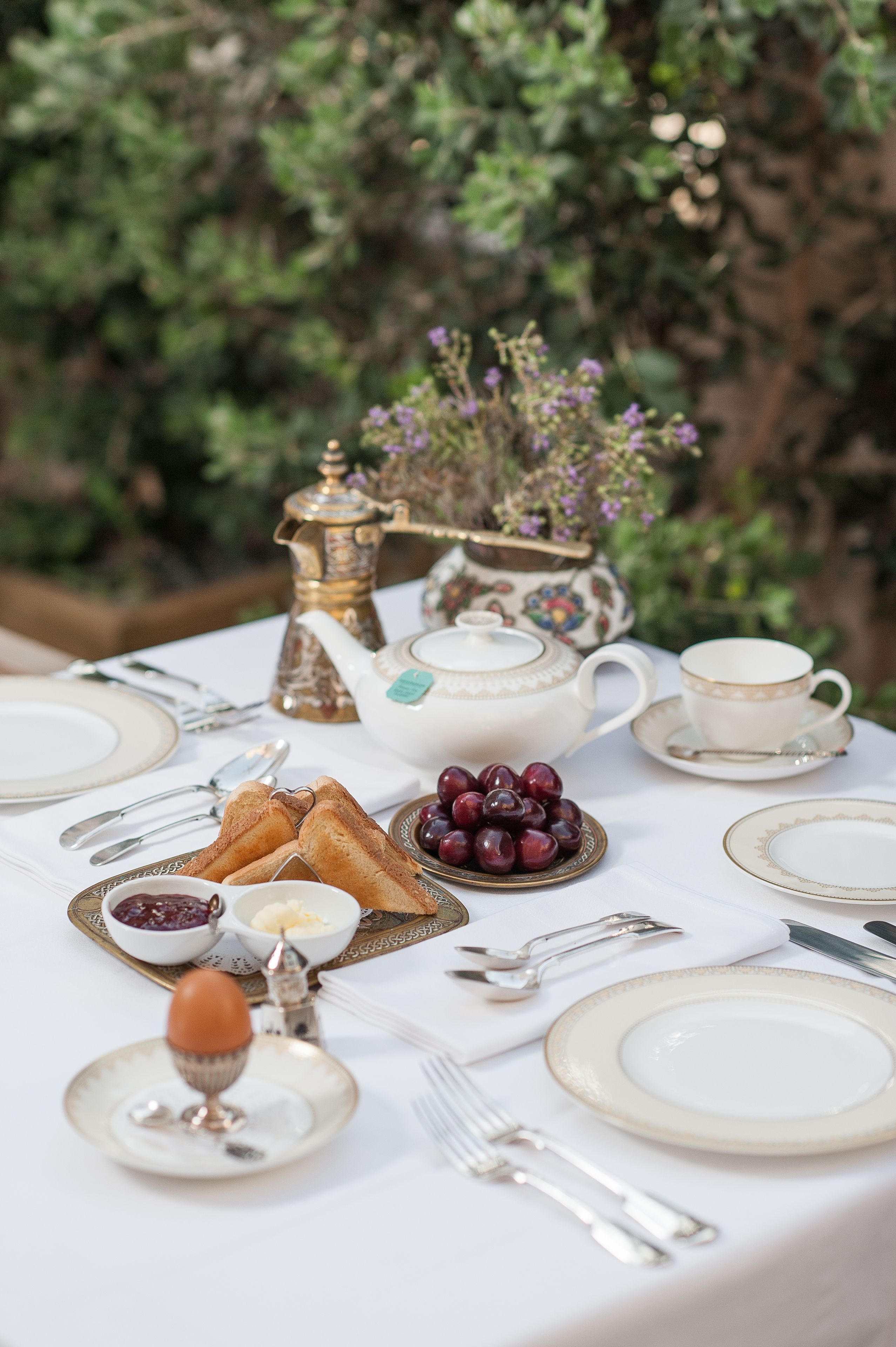 A table set for a meal with a teapot, cups, plates, and a variety of food items.