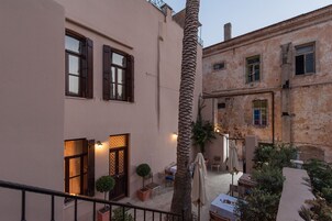 Un cortile con una palma, posti a sedere all'aperto e un edificio con un balcone.