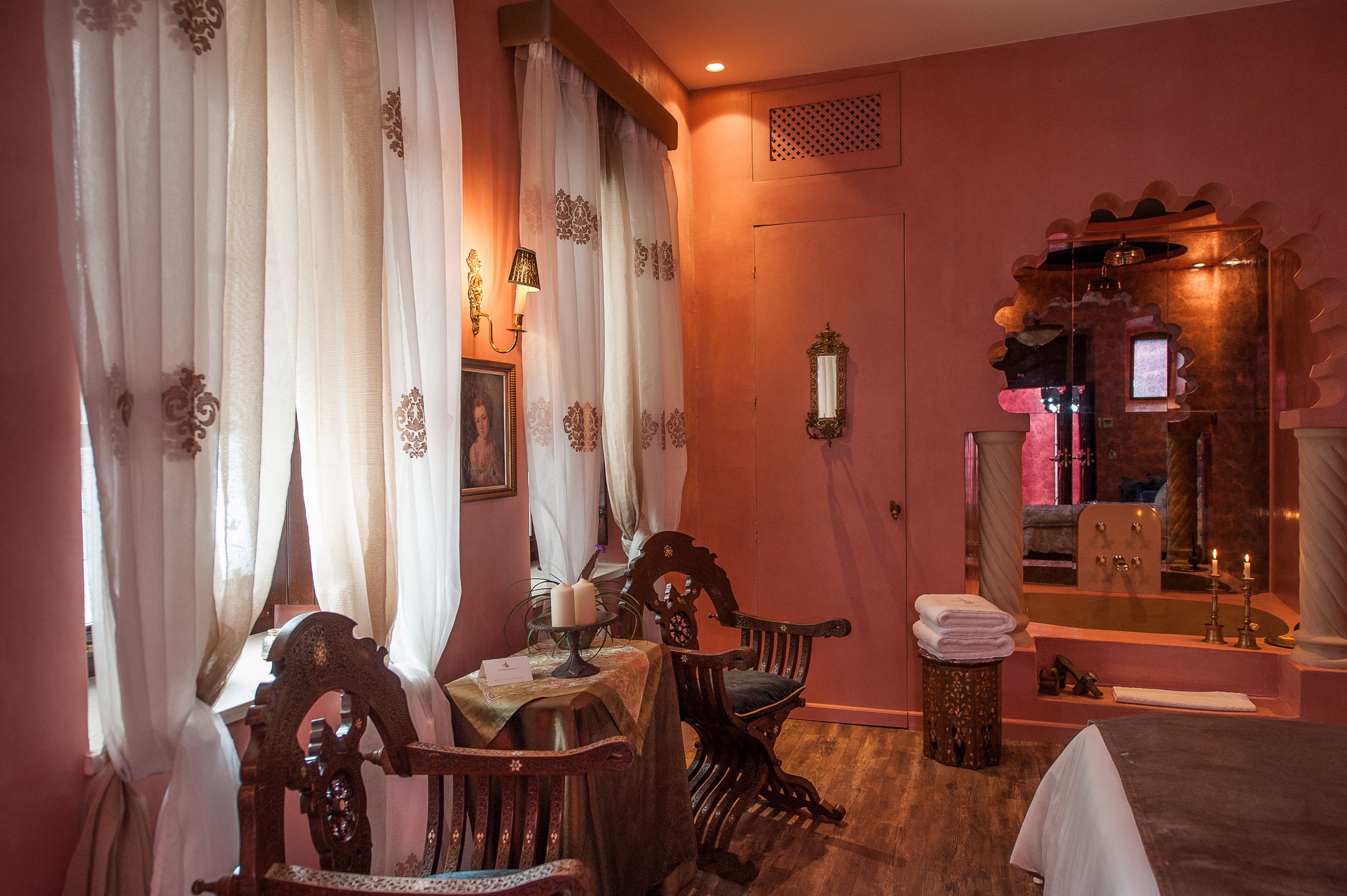 A room with a wooden chair, a table with a candle, a mirror, and a bathtub.