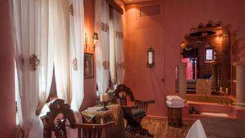 A room with a wooden chair, a table with a candle, a mirror, and a bathtub.