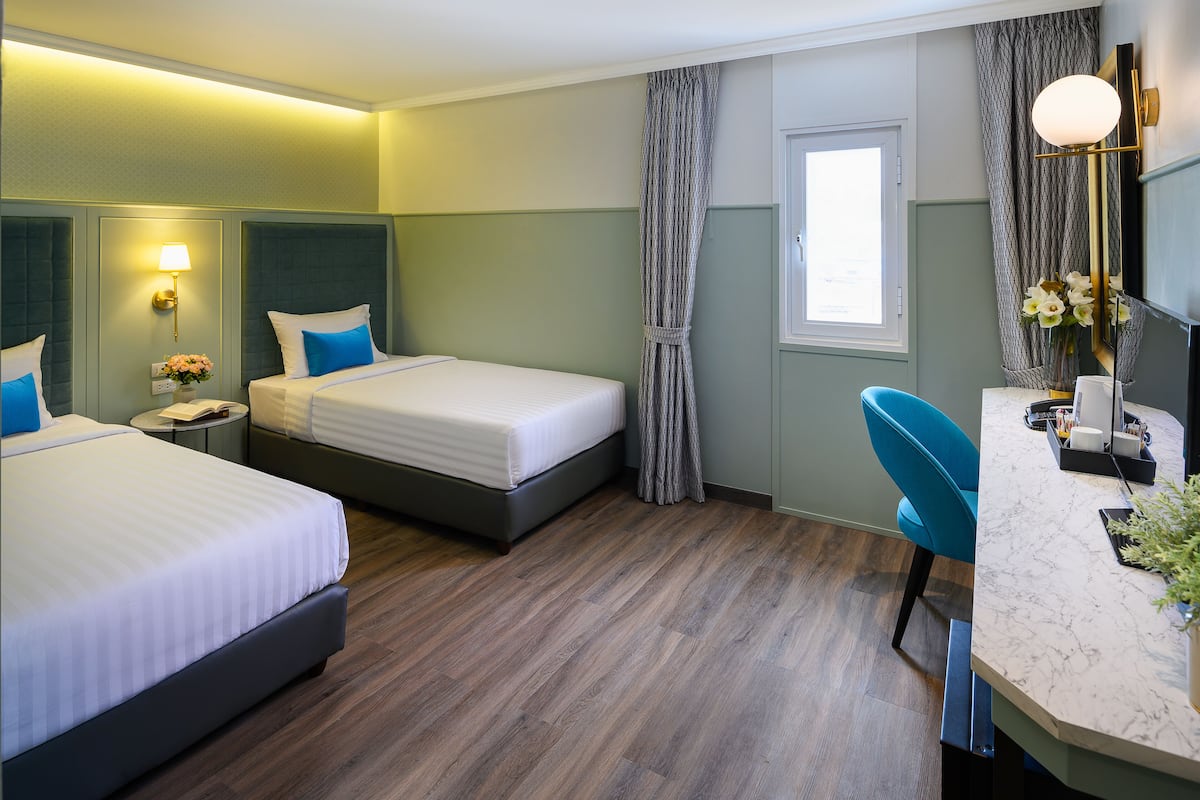 A hotel room with two beds, a desk, a chair, a nightstand, and a window.