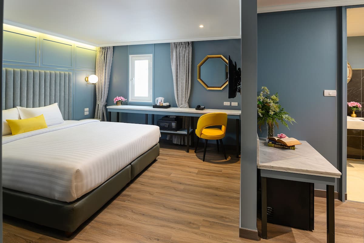 A modern hotel room with a large bed, a desk, a chair, and a small table with a plant.