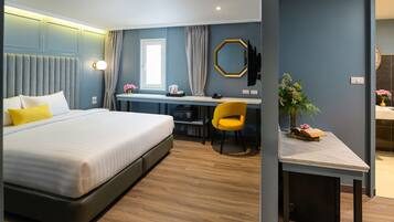 A modern hotel room with a large bed, a desk, a chair, and a small table with a plant.