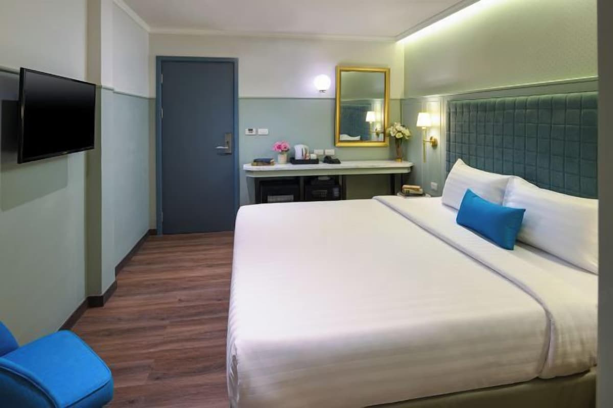 A hotel room with a bed, a desk, a chair, a television, and a mirror.