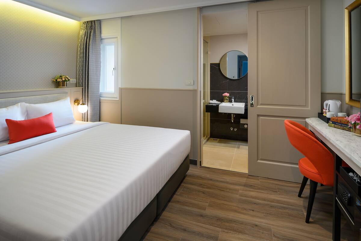 A hotel room with a bed, a desk, and a bathroom visible through an open door.