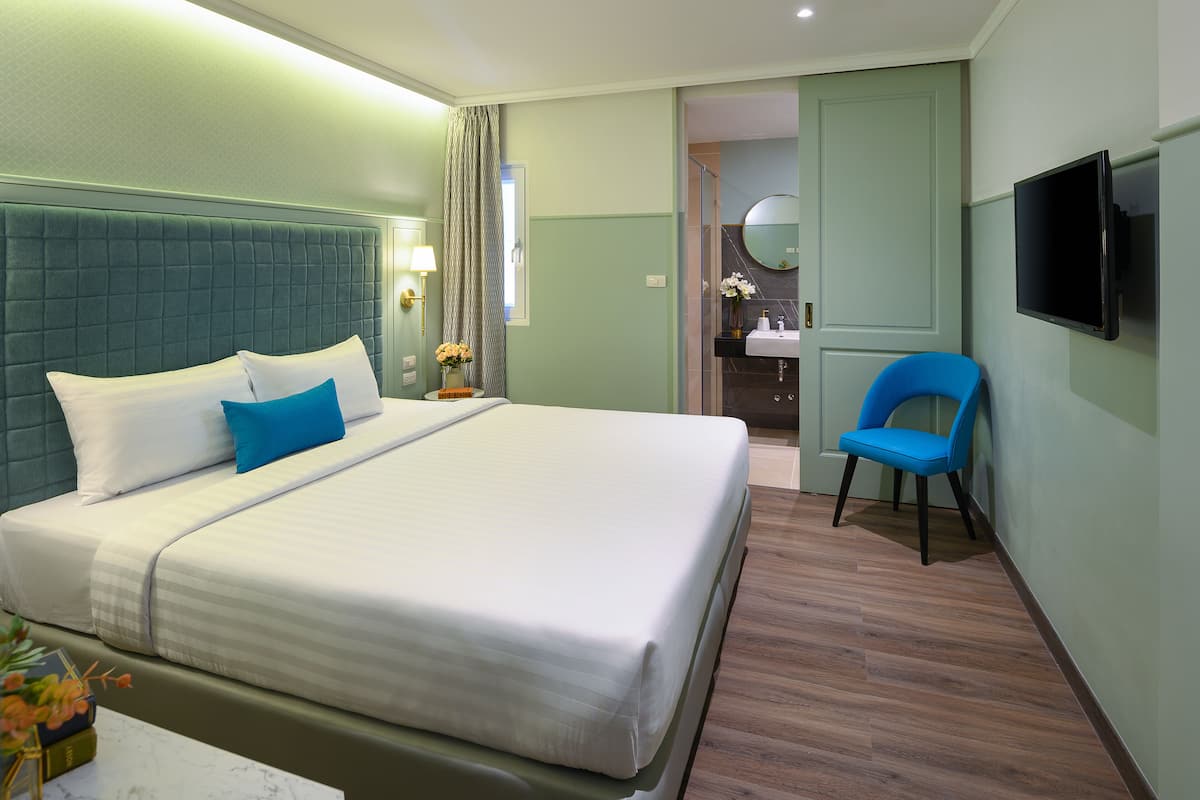 A hotel room with a large bed, a chair, a TV, and a bathroom visible through an open door.