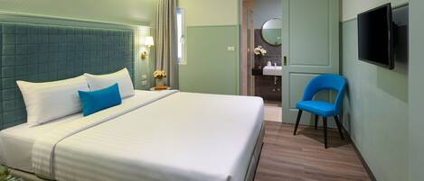 A hotel room with a large bed, a chair, a TV, and a bathroom visible through an open door.