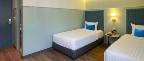A hotel room with two beds, a small table with a lamp, and a door.