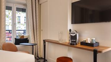 Quarto de hotel com cama, uma mesinha com cafeteira, televisão na parede e janela com cortinas.