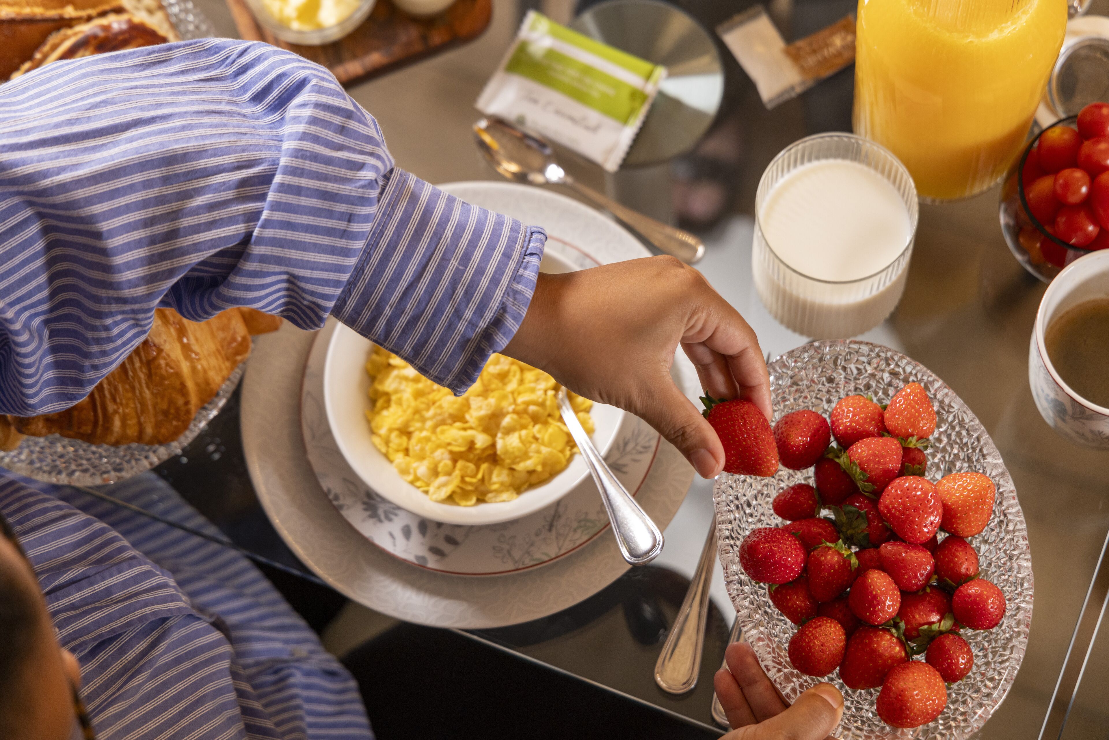 A breakfast setting with a bowl of cereal, a plate of strawberries, and a glass of orange juice.