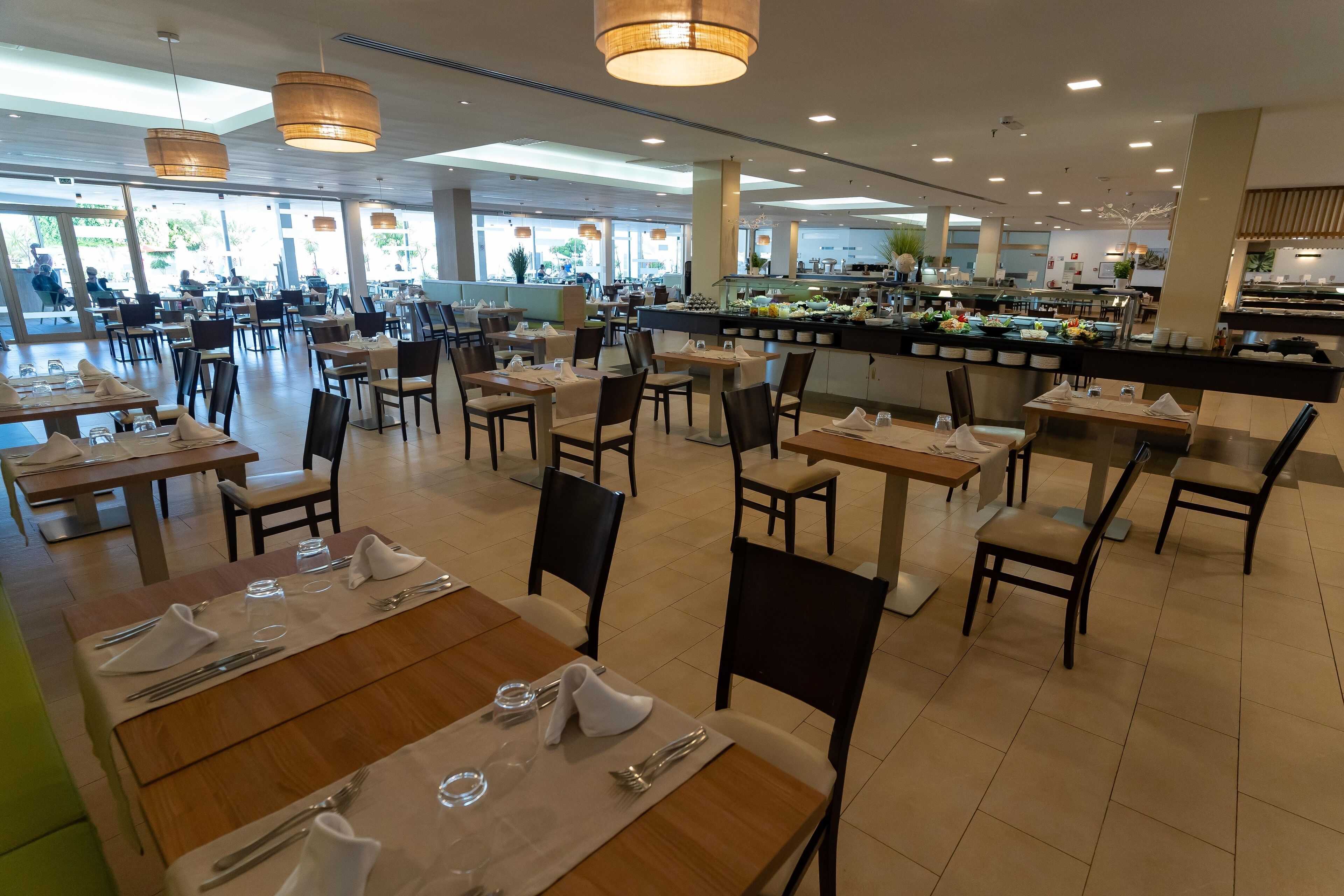 Een ruime eetruimte met meerdere tafels en stoelen, een buffet en grote ramen voor natuurlijk licht.