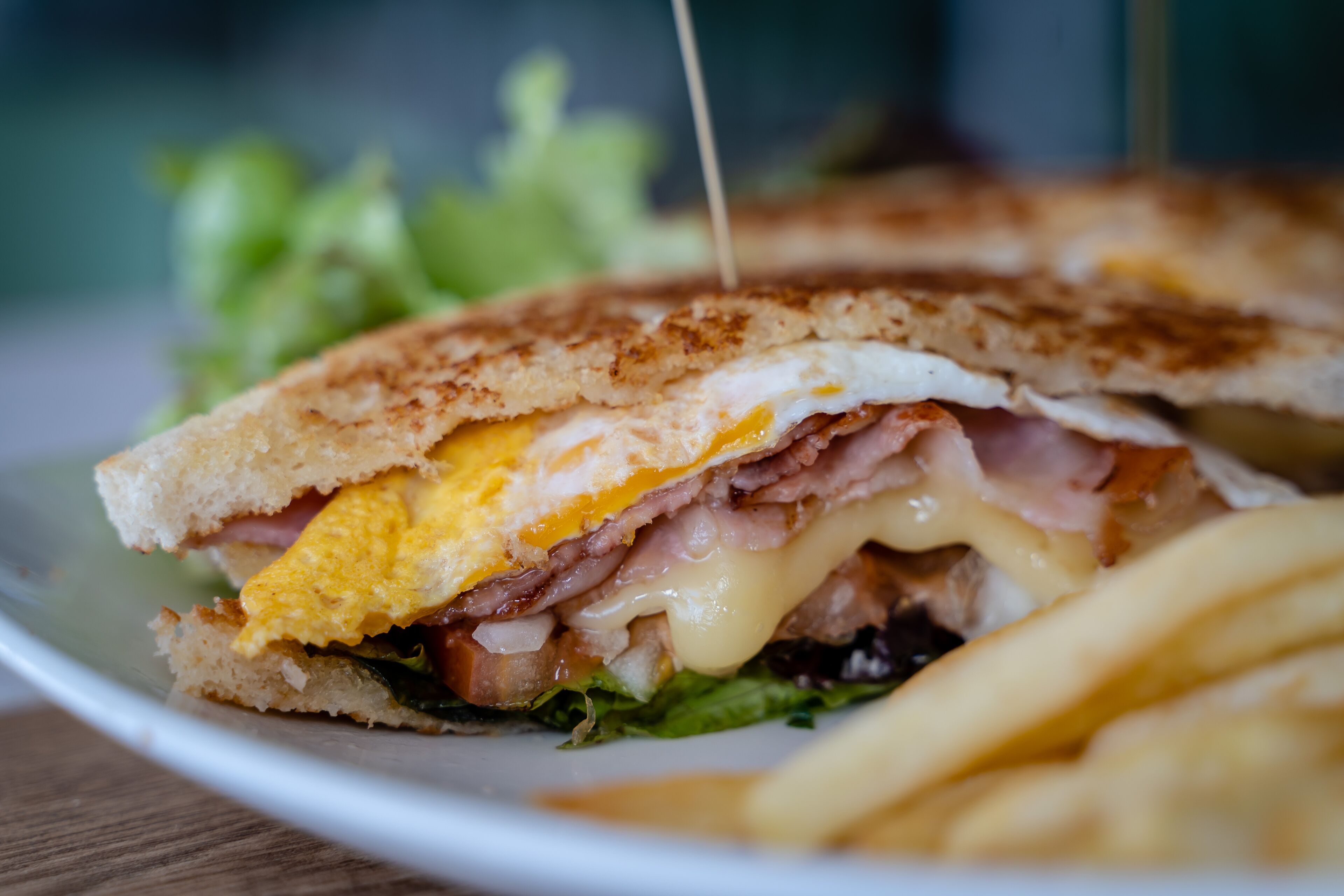 Sándwich con capas visibles de huevo, jamón, queso y lechuga, servido en un plato con papas fritas.