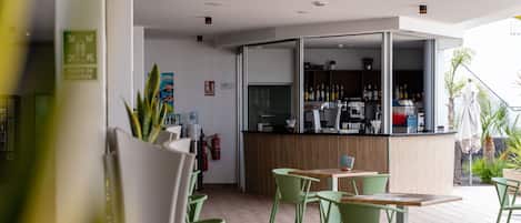 Un café moderno con sillas y mesas verdes, una barra de madera con una máquina de café y vistas al exterior.