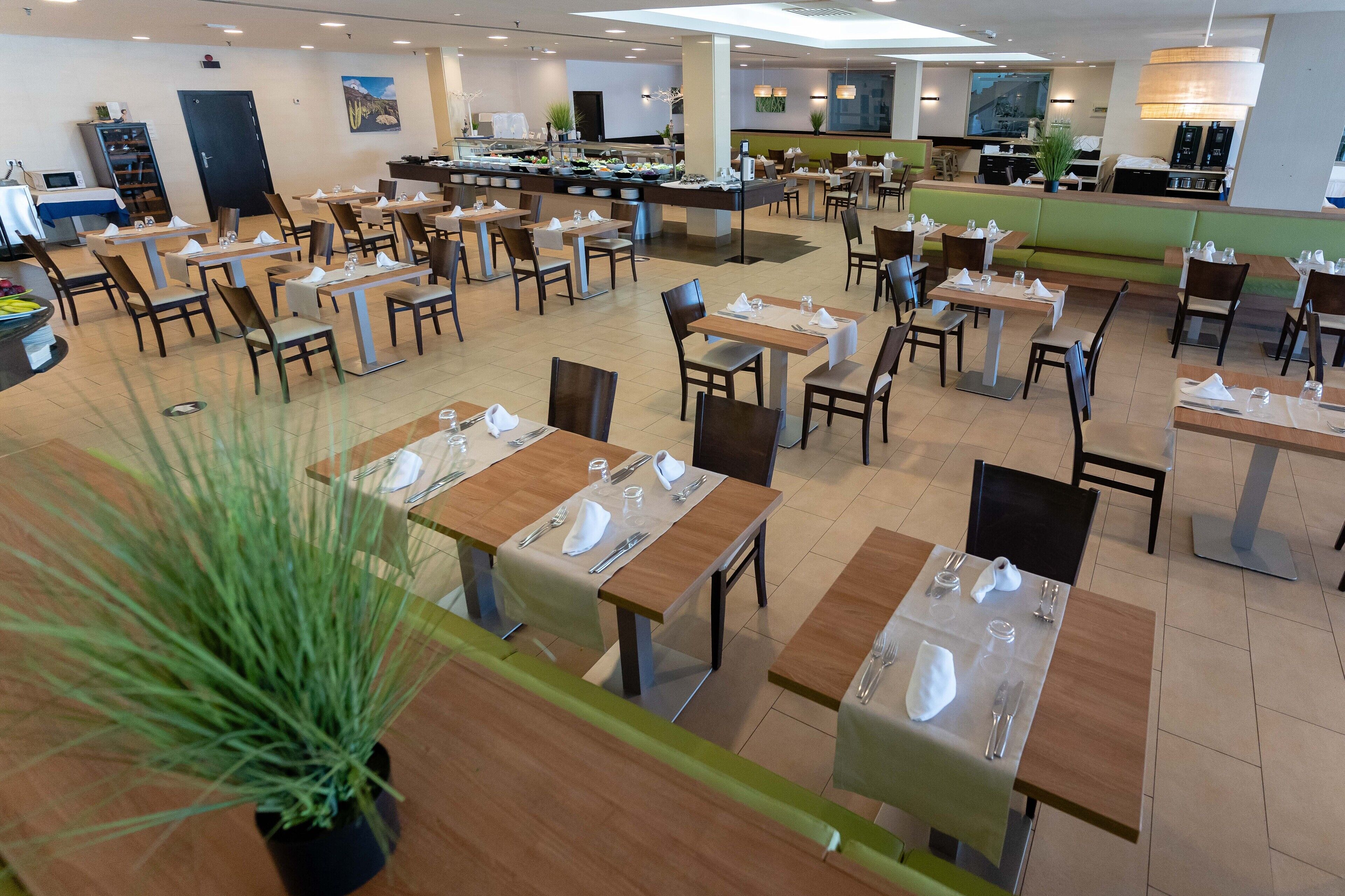 A spacious dining area with multiple tables and chairs, a buffet counter, and a variety of plants.