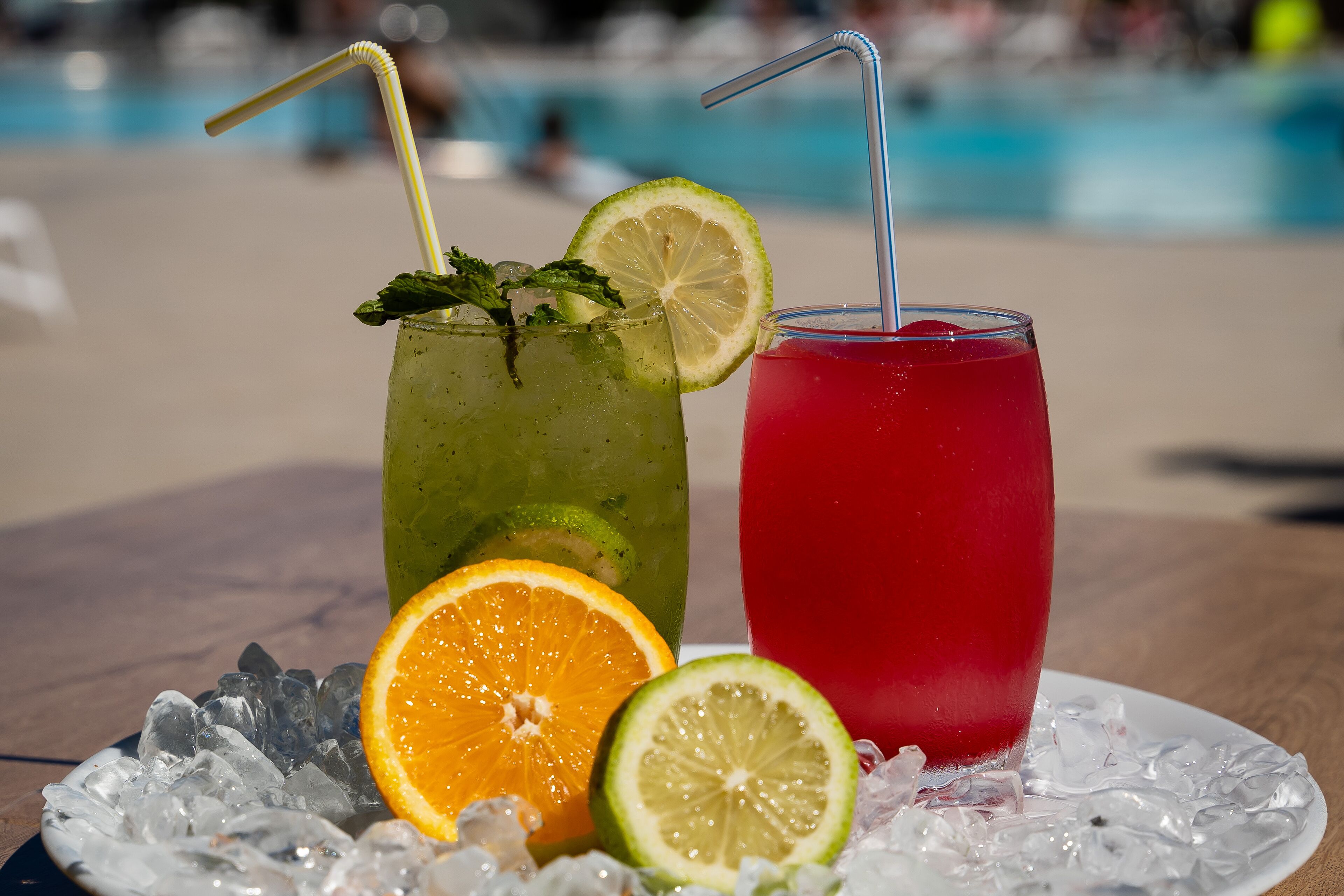 Two drinks on a table with ice and fruit slices.