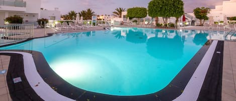 Una piscina con borde de baldosas, rodeada de sillas de descanso y palmeras.