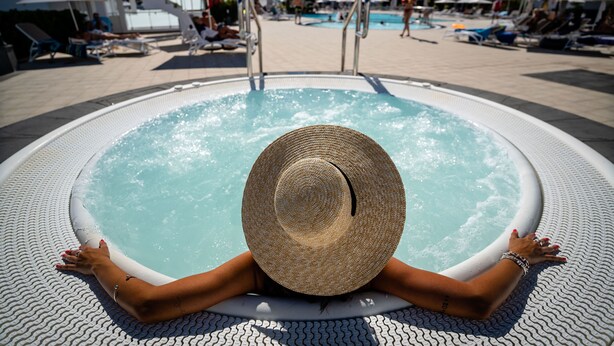 Una persona relajándose en un jacuzzi con vistas a una piscina y sillones de descanso.
