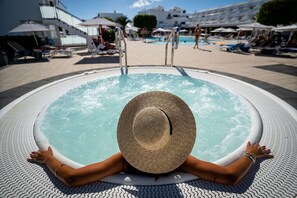 A person relaxing in a hot tub with a view of a pool area and lounge chairs. - Hotel Lanzarote Village (Tías)