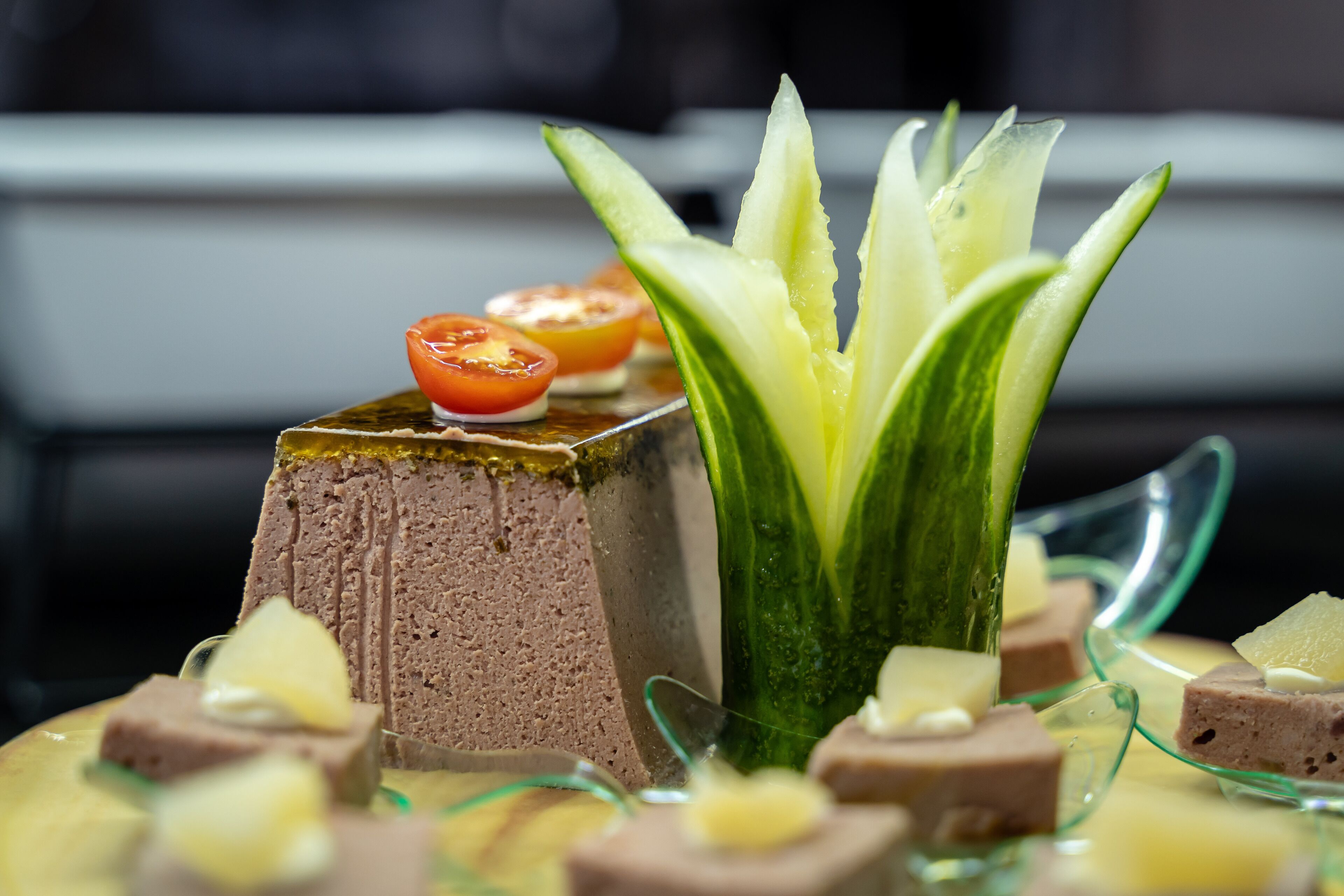 A dessert plate with a layered cake, a cucumber garnish, and small fruit pieces.