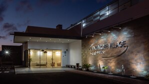 Una entrada de hotel moderna con puerta de cristal, un letrero que dice 'LANZAROTE VILLAGE Hotel' y una fachada bien iluminada.