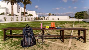 A tennis court with a picnic table, a tennis racket, and balls.