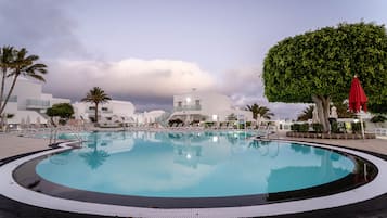 Une piscine à bord arrondi, entourée de chaises longues et de parasols, avec des bâtiments modernes en arrière-plan.